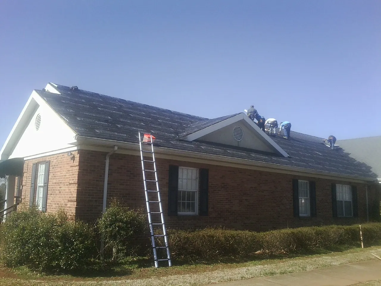 Crew tearing shingles off a brick ranch roof with a ladder set — Metal Roof Repair work by our crew in Readsboro