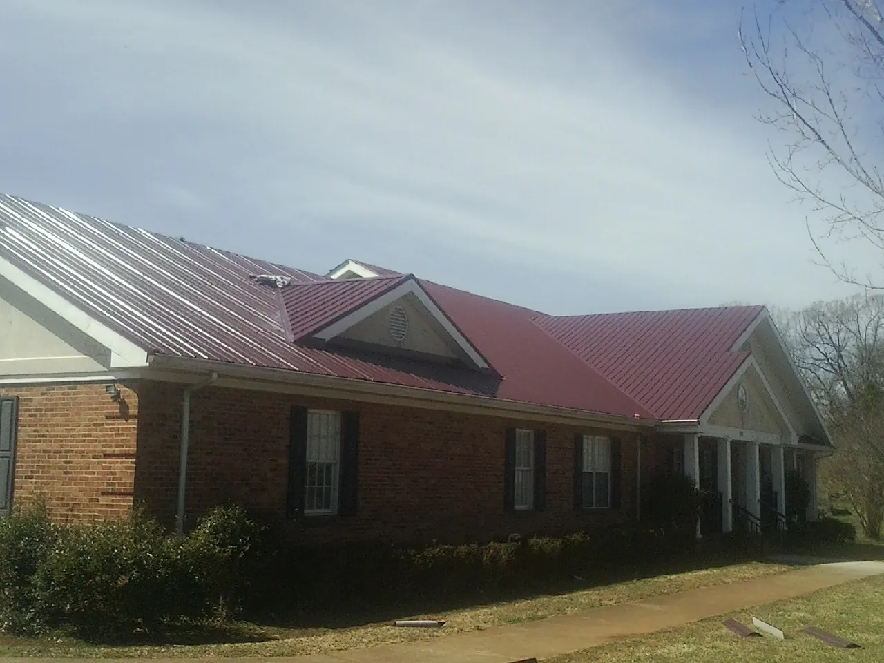 Red metal roof with gabled entries on a long brick building, from a Hail Damage Roof Repair job in Readsboro