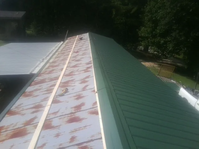 Old rusted panels beside newly installed green metal roofing in Readsboro