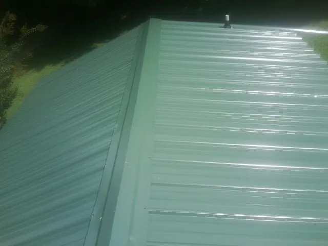 New green metal panels meeting at the ridge of a roof — Flat Roof Repair work by our crew in Readsboro