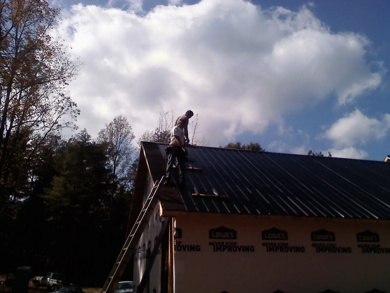 Roofer fastening dark metal panels high against a cloudy sky, from a Roof Inspection job in Readsboro