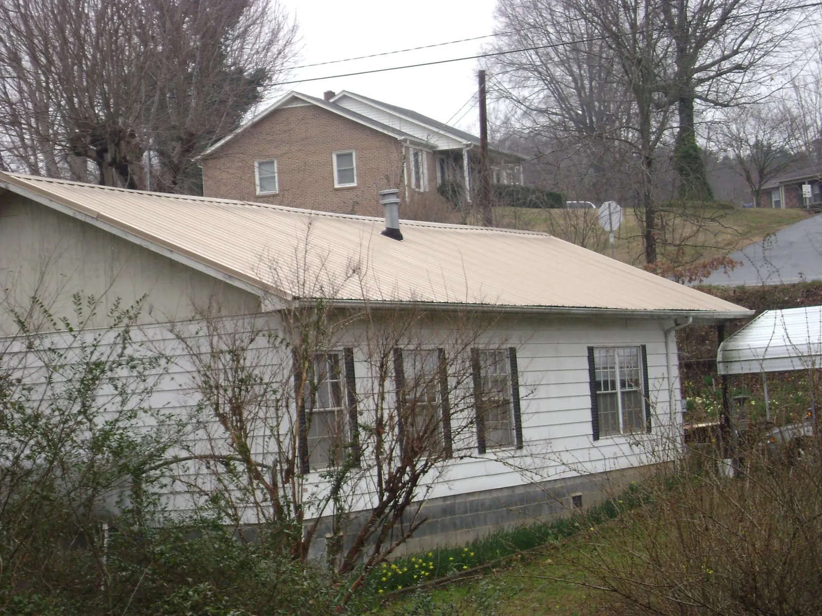 Tan metal roof on a white sided house set into a hillside — Commercial Roofing by Roofing Brothers in Readsboro